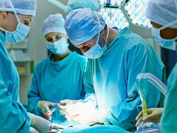 Equipe médica usando máscaras e roupas próprias faz uma cirurgia em paciente em um hospital.